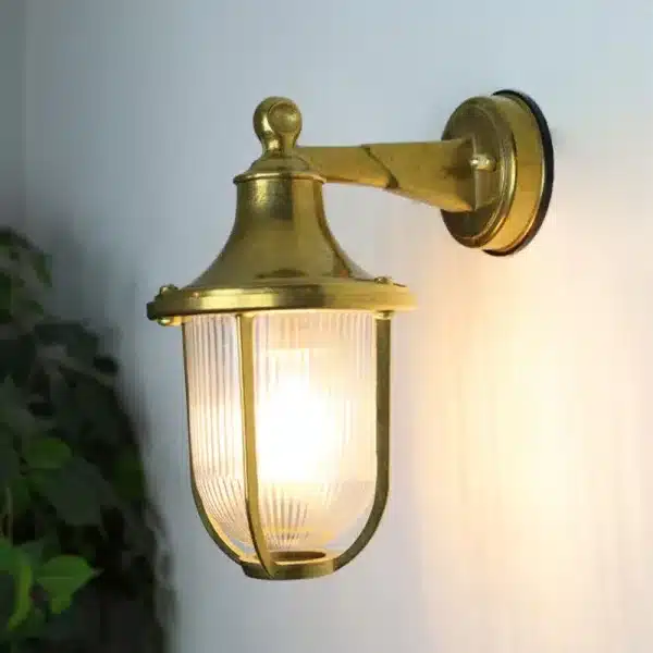 Brass down coastal outdoor wall light illuminated in garden