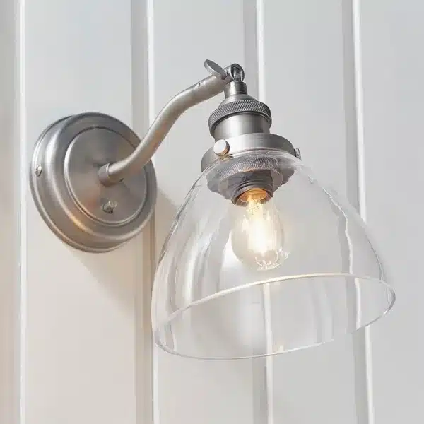 Close-up of brushed silver wall light with clear glass shade lit